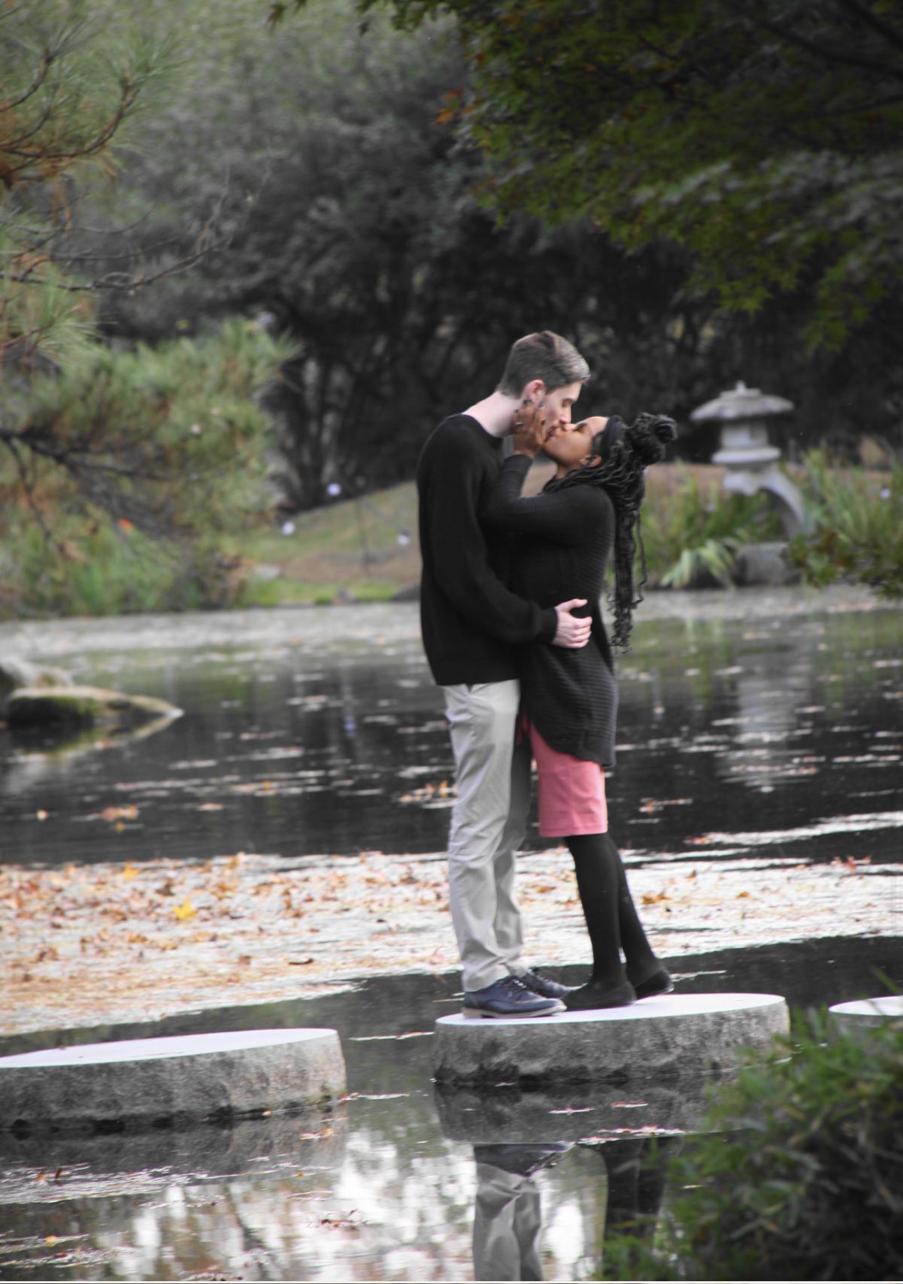 Engaged couple kissing on stepping stones over a garden pond in autumn