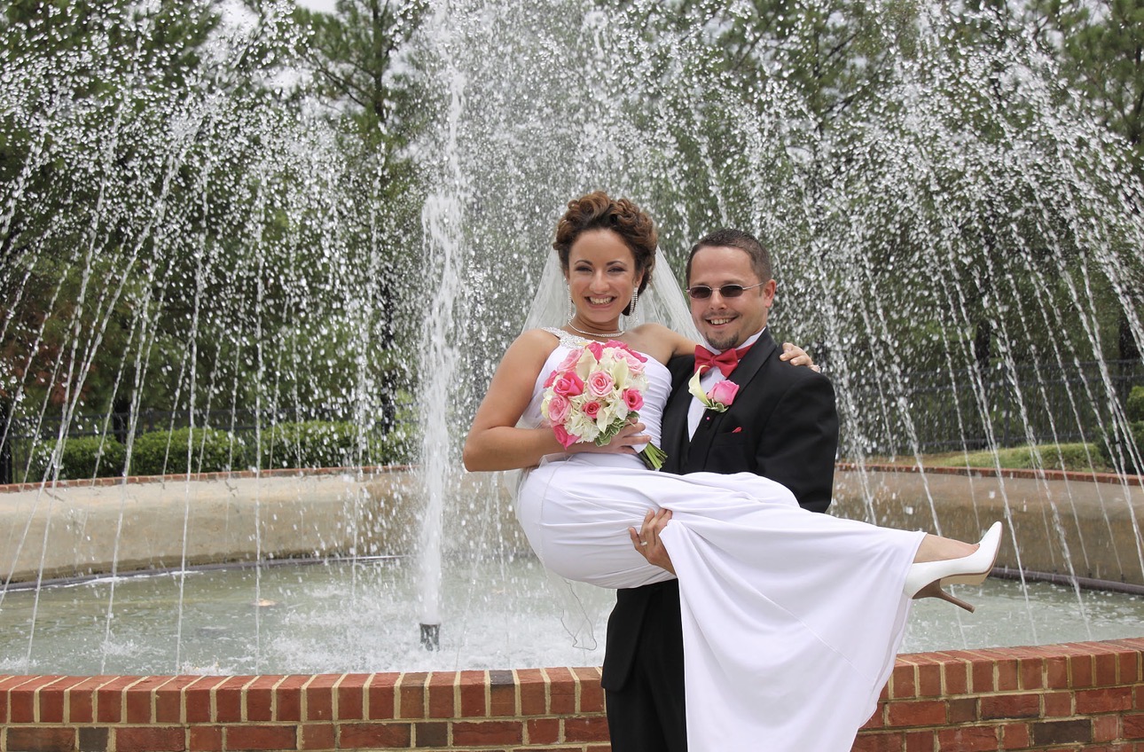 Groom lifting his bride in his arms in front of a large garden fountain