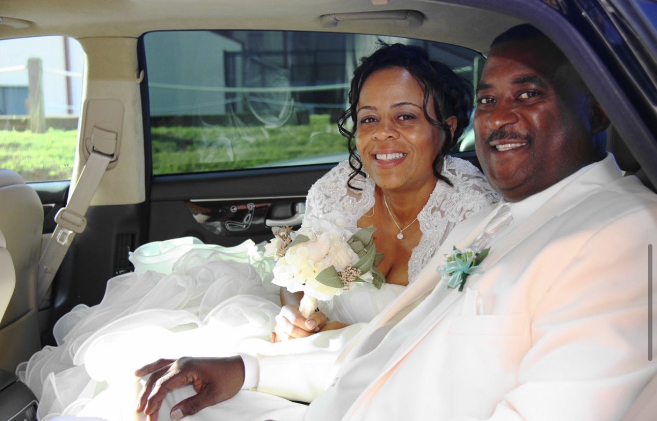 Bride and groom seated together in the car, smiling, bouquet in her lap