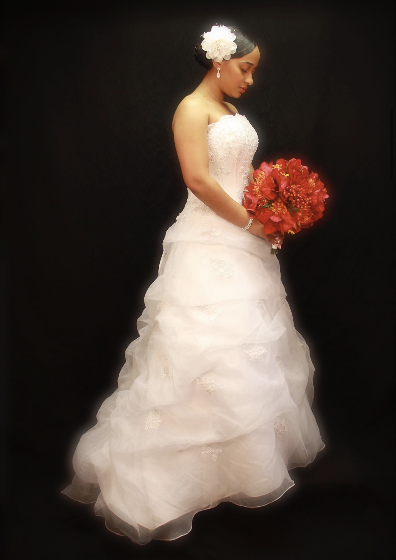 Bride in a full organza gown holding a red bouquet, photographed against a black studio backdrop